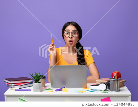 Idea Concept. Excited Young Indian Woman In Eyeglasses Sitting At The Desk Using Laptop And Raising Pencil Up Isolated Over Purple Background In Studio. Amazed Shocked Lady Having Insight, Aha Moment. 124044953