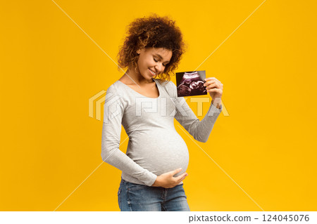Happy afro pregnant woman with her baby sonography, enjoying first photo of her unborn child, pink background Happy afro pregnant woman with her baby sonography, enjoying first photo of her unborn child, pink background 124045076