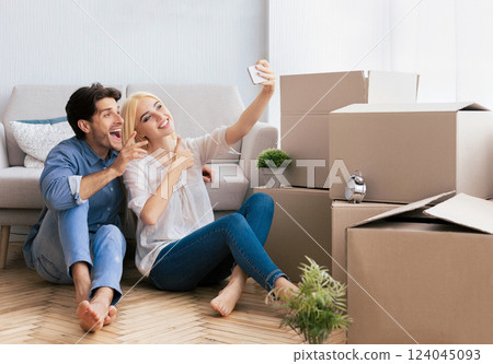A couple smiles for a selfie as they sit among moving boxes in their new home. A couple smiles for a selfie as they sit among moving boxes in their new home. 124045093
