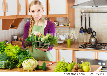 Woman in kitchen having vegetables holding shopping basket Woman in kitchen having vegetables holding shopping basket 124045491