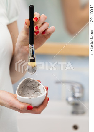 Female hand holding clay mud mask and brush. Skin care. 124045514