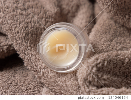 Opened lip balm jar on brown bath towel closeup. Herbal cosmetic product for daily lipcare 124046154