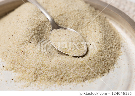 Plate of raw uncooked fonio seeds with a metal spoon closeup. African ancient pseudocereal 124046155