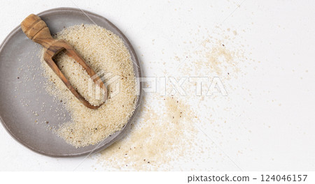 Raw uncooked fonio seeds on grey plate with a wooden scoop on white table topview. African cereal Raw uncooked fonio seeds on grey plate with a wooden scoop on white table topview. African cereal 124046157