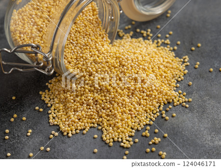 Glass jar of raw yellow pearl hulled millet grain on grey table closeup. Ancient food 124046171