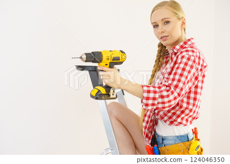 Woman on ladder using drill 124046350