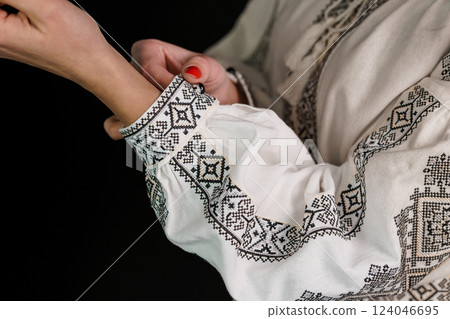 Close-up of Woman's Hands Adjusting Traditional Embroidered White Garment Sleeve with Black Geometric Patterns 124046695