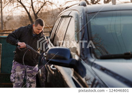 Man Thoroughly Cleaning Vehicle Exterior Using Pressure Washer Outdoors 124046801
