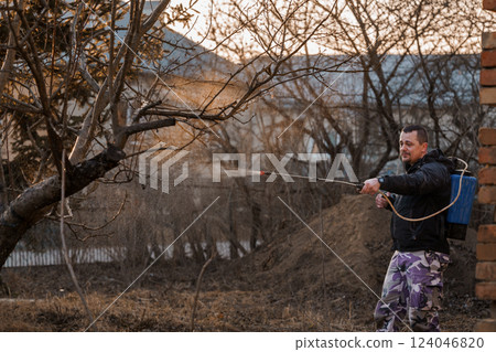 Man Spraying Tree Branches with Pesticide in Evening Garden Setting 124046820