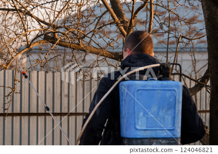 Person Spraying Fruit Trees Using Portable Blue Garden Spray Equipment in Early Springtime Person Spraying Fruit Trees Using Portable Blue Garden Spray Equipment in Early Springtime 124046821
