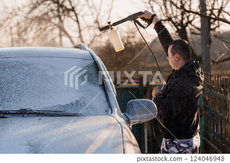 Man Washing Car with High-Pressure Washer Outdoor During Sunset Time 124046948