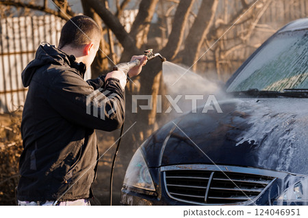 Man Washing Car Outdoors with High Pressure Water Spray in Sunlight Man Washing Car Outdoors with High Pressure Water Spray in Sunlight 124046951