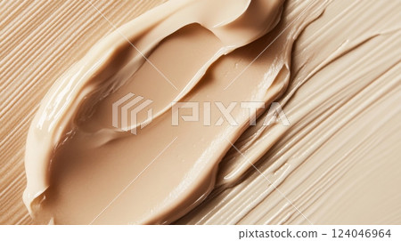 A creamy foundation swatch is artfully spread over a textured beige surface, highlighting its smooth consistency and natural hue. This visual captures the essence of makeup application techniques. 124046964