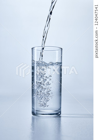 Close-up photo of transparent water being poured into a clear, cylindrical glass, showing bubbles and splashes, against soft background. Mock up. Close-up photo of transparent water being poured into a clear, cylindrical glass, showing bubbles and splashes, against soft background. Mock up. 124047541