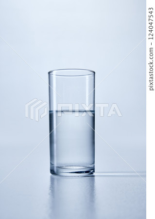 Close-up photo of clear, cylindrical glass filled with transparent water, against soft blue background. Mock up Close-up photo of clear, cylindrical glass filled with transparent water, against soft blue background. Mock up 124047543