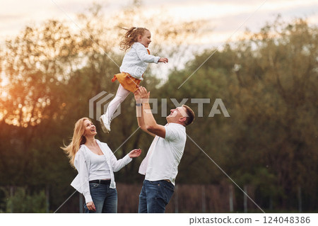 Throwing girl up and catching by the hands. Family have weekend outdoors at summertime together Throwing girl up and catching by the hands. Family have weekend outdoors at summertime together 124048386