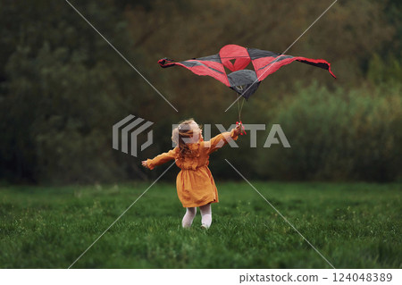 Having fun. Little girl is running with red colored kite outdoors. Playful mood 124048389