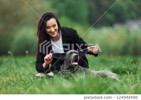 Playful mood. Holding by the ears. Young brunette is having a walk with her dog outdoors Playful mood. Holding by the ears. Young brunette is having a walk with her dog outdoors 124048480