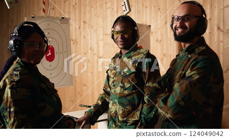 Portrait of happy army soldiers in shooting gallery looking at targets, comparing points obtained. Cheerful military units testing accuracy in firing range, looking at shot bullseye, camera A 124049042