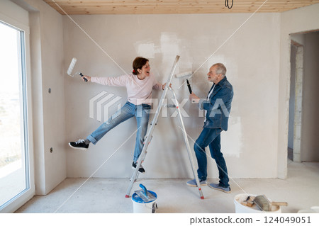 Senior husband and wife standing on a ladder repainting the walls. Senior husband and wife standing on a ladder repainting the walls. 124049051