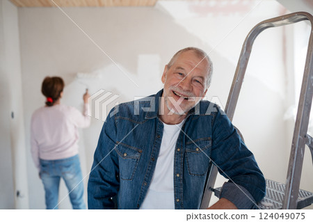 Senior man painting walls in new home, looking at camera. Senior man painting walls in new home, looking at camera. 124049075