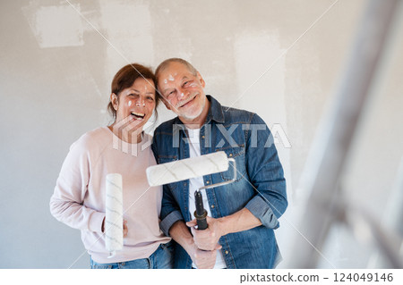 Senior couple painting walls with roller in new home, looking at camera. 124049146