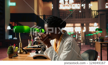 University scholar focuses on examining chemical processes and microorganisms for medical science career. Woman studying in the library to support her educational development. Camera A. University scholar focuses on examining chemical processes and microorganisms for medical science career. Woman studying in the library to support her educational development. Camera A. 124049167