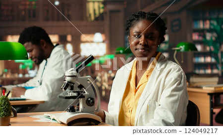 University scholar focuses on examining chemical processes and microorganisms for medical science career. Woman studying in the library to support her educational development. Camera B. 124049217