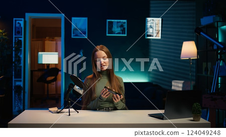 Tech specialist filming technology review of newly launched smartphone, presenting features to subscribers. Influencer advertising mobile phone to fans from home studio, camera B 124049248