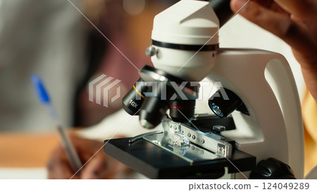 University student prepares for exam by researching cells and microorganisms under the microscope. Using books and papers from the academic database in the college library. Close up. Camera B. 124049289