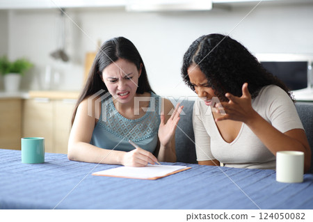 Angry interracial roommates reading a contract in the kitchen Angry interracial roommates reading a contract in the kitchen 124050082