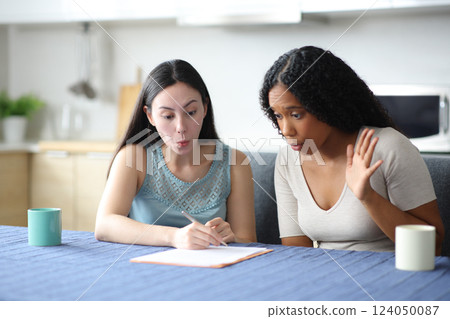 Surprised interracial roommates reading a contract at home 124050087