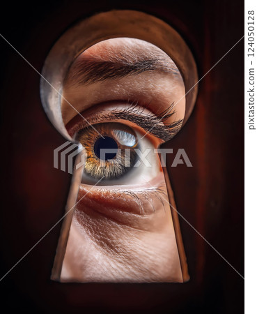 Hidden secrets curiosity or spying concept. Woman eye looking through a keyhole as peeking to see unknown information. Person behind the door sneaks and lurks. Closeup eyeball peering into key hole 124050128