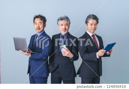 Group of middle-aged male business people holding various digital devices Group of middle-aged male business people holding various digital devices 124050410