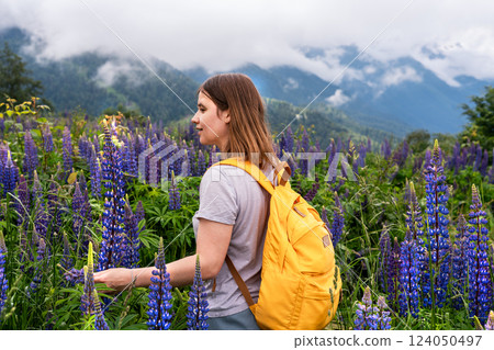 charming female traveler explores blooming meadow full of vibrant blue purple lupines lupine flowers, enjoying beauty of nature in the mountains, touching blossoming flowers, eco tourism charming female traveler explores blooming meadow full of vibrant blue purple lupines lupine flowers, enjoying beauty of nature in the mountains, touching blossoming flowers, eco tourism 124050497