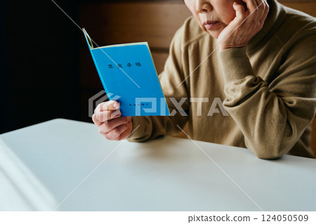 A senior woman resting her chin on her hand and looking at her pension book A senior woman resting her chin on her hand and looking at her pension book 124050509