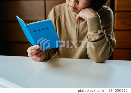 A senior woman resting her chin on her hand and looking at her pension book A senior woman resting her chin on her hand and looking at her pension book 124050511