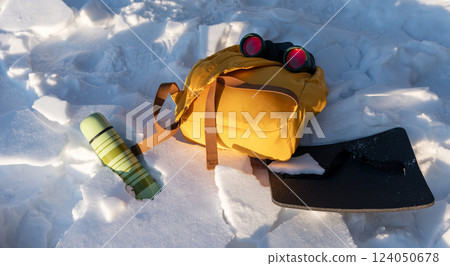 Equipment of a birdwatcher or ornithologist ecologist - a thermos, binoculars and a backpack lying on the snow Equipment of a birdwatcher or ornithologist ecologist - a thermos, binoculars and a backpack lying on the snow 124050678
