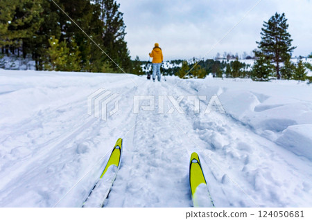 yellow skis on the snow and a woman skier in defocus in front. Skiing in the forest. Winter sports and active lifestyle, hiking and tourism. 124050681