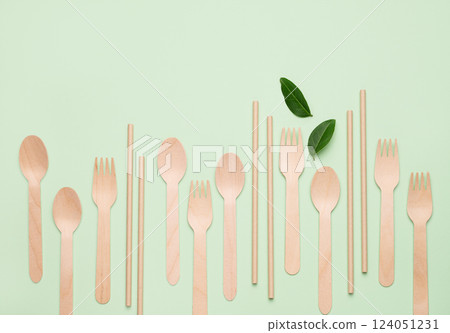 Flat lay wooden spoons, forks and straw on green background with leaves. Flat lay wooden spoons, forks and straw on green background with leaves. 124051231