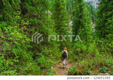 girl with black backpack walks through forest thicket in Almaty. path in coniferous thickets 124051395