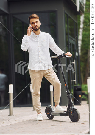 Talking by phone. Stylish man is with his scooter outdoors at daytime 124052130