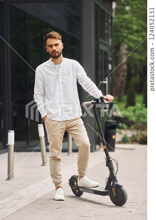 Posing for a camera. Stylish man is with his scooter outdoors at daytime Posing for a camera. Stylish man is with his scooter outdoors at daytime 124052131