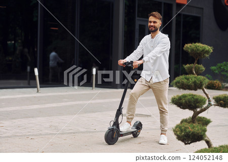 Riding the scooter. Stylish man is outdoors at daytime Riding the scooter. Stylish man is outdoors at daytime 124052148