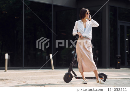 Using phone. Beautiful young woman is with her scooter outdoors Using phone. Beautiful young woman is with her scooter outdoors 124052211