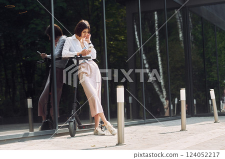 Online messaging. Beautiful young woman is with her scooter outdoors Online messaging. Beautiful young woman is with her scooter outdoors 124052217