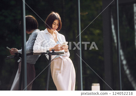 Online messaging. Beautiful young woman is with her scooter outdoors Online messaging. Beautiful young woman is with her scooter outdoors 124052218
