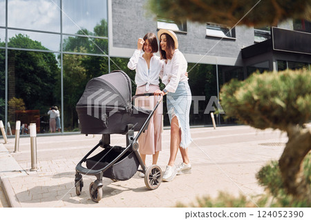 Talking and having fun. Two female friends having a walk with baby carriage outdoors Talking and having fun. Two female friends having a walk with baby carriage outdoors 124052390