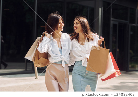 Happy buyers. Two female friends have a shopping day. Walking outdoors with bags Happy buyers. Two female friends have a shopping day. Walking outdoors with bags 124052402