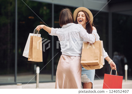 Smiling and talking. Two female friends have a shopping day. Walking outdoors with bags 124052407